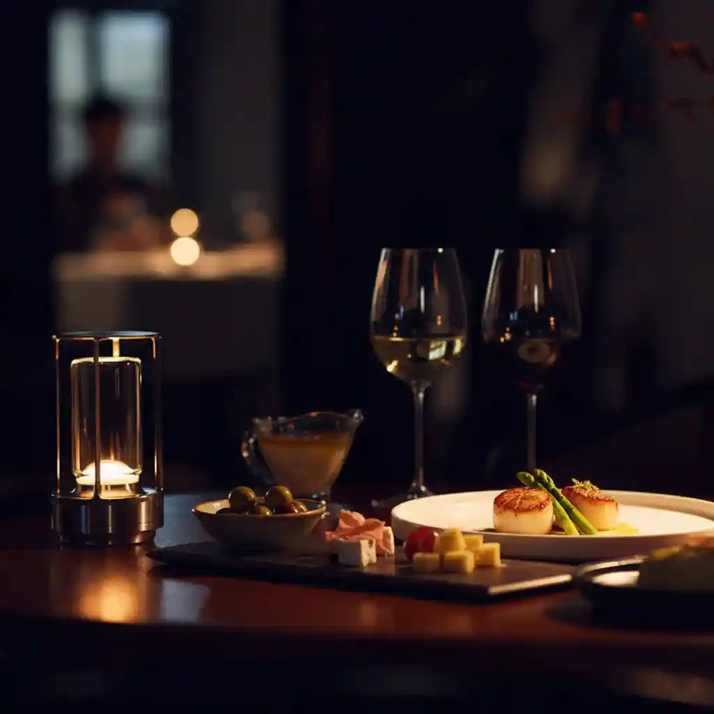Dinner setting with wine glasses, candles, and food on a table in a dimly lit room.