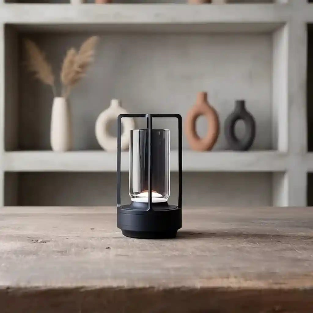 Black cylindrical lamp on a wooden surface with a blurred background of decorative vases.